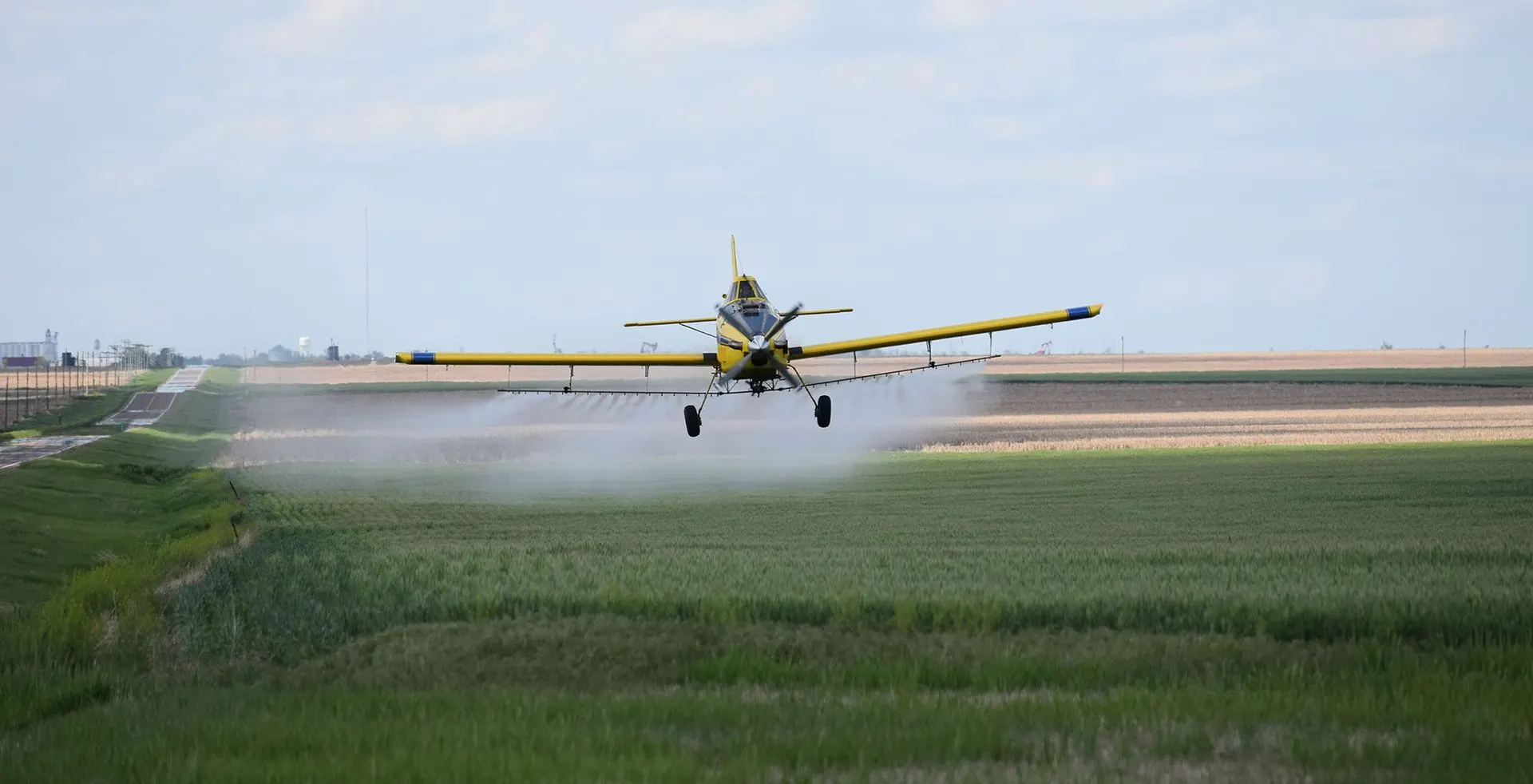 Crop-duster flying low over a green field, leaving a white spray trail