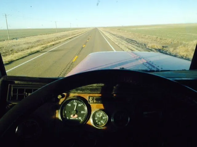 View from a truck cab down a straight two-lane highway across flat farmland