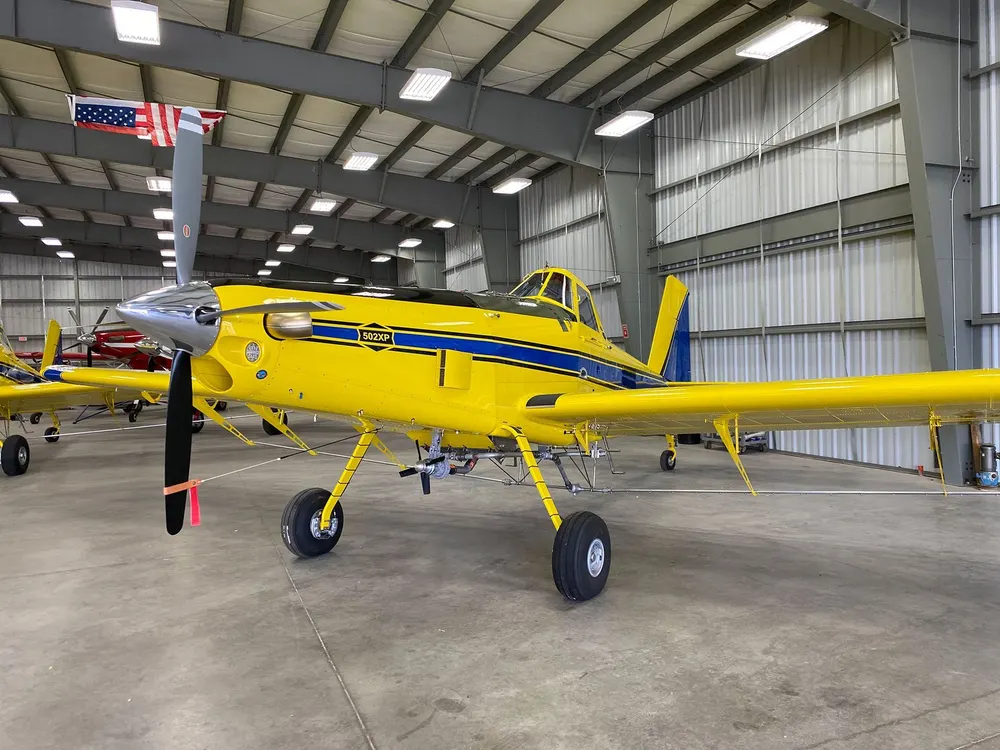 Yellow spray plane parked inside a bright metal hangar