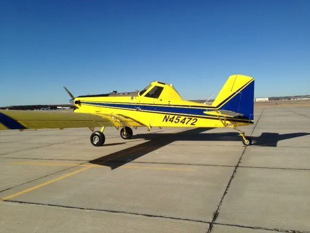 Yellow and blue spray plane parked on a concrete ramp under a clear sky