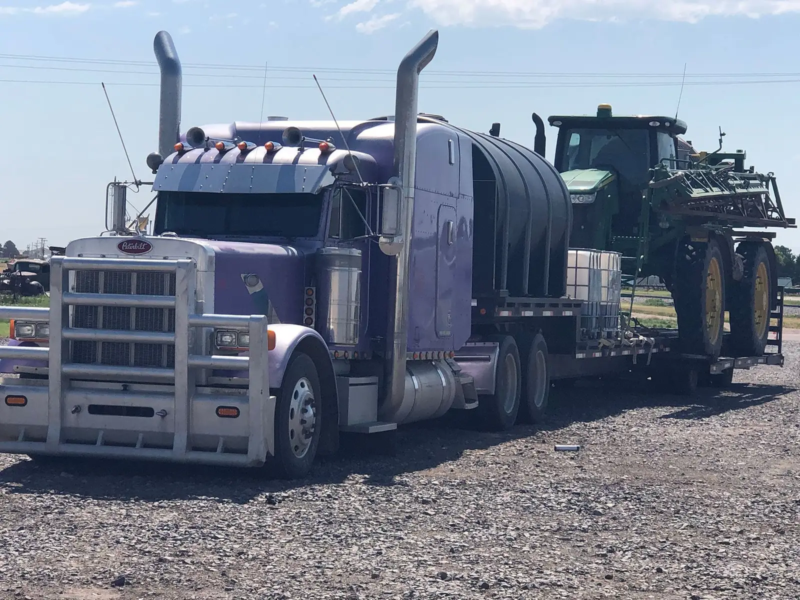 Semi truck hauling a large tank and a green sprayer on a trailer